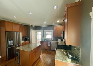 Kitchen featuring appliances with stainless steel finishes, a sink, a center island, light stone counters, and tasteful backsplash
