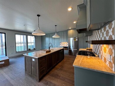 Kitchen with backsplash, light stone counters, hanging light fixtures, freestanding refrigerator, and dark wood-style flooring