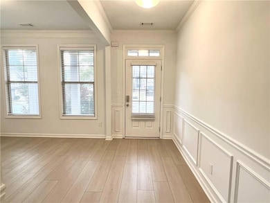 Doorway featuring crown molding, wainscoting, wood finished floors, and a decorative wall