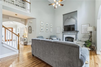 Living area featuring arched walkways, ceiling fan, a high ceiling, a fireplace, and wood finished floors