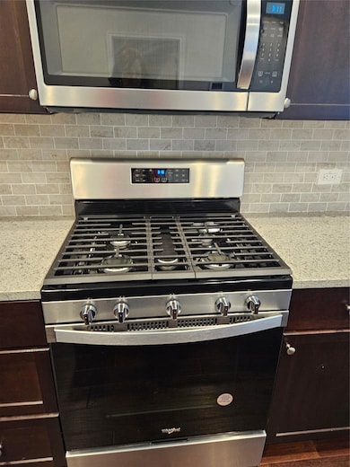 Kitchen view of dark brown cabinetry, stainless steel gas range oven, and backsplash