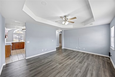 Unfurnished room with a tray ceiling, ceiling fan, and dark wood-style floors