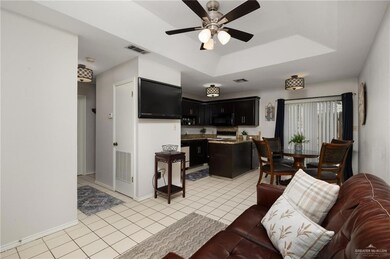 Living area with light tile patterned flooring, visible vents, a raised ceiling, and a ceiling fan