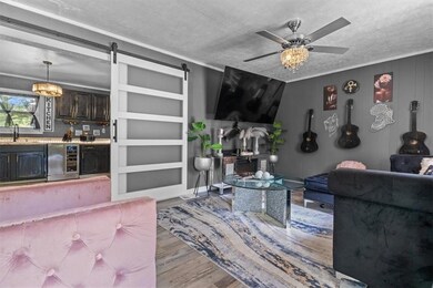 Living room featuring wood finished floors, a barn door, a textured ceiling, ceiling fan, and wine cooler