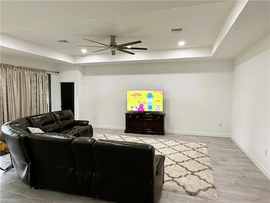 Living room featuring a raised ceiling, ceiling fan, and recessed lighting