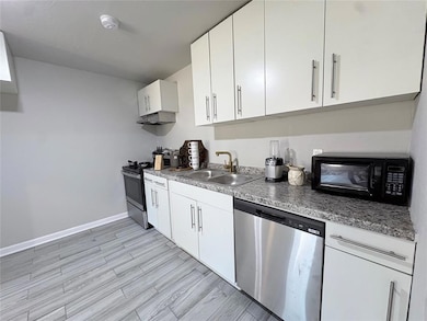 Kitchen with appliances with stainless steel finishes, white cabinetry, light wood finished floors, and under cabinet range hood