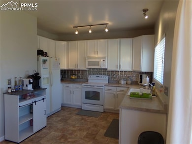 Kitchen with white appliances, white cabinetry, tasteful backsplash, and light countertops