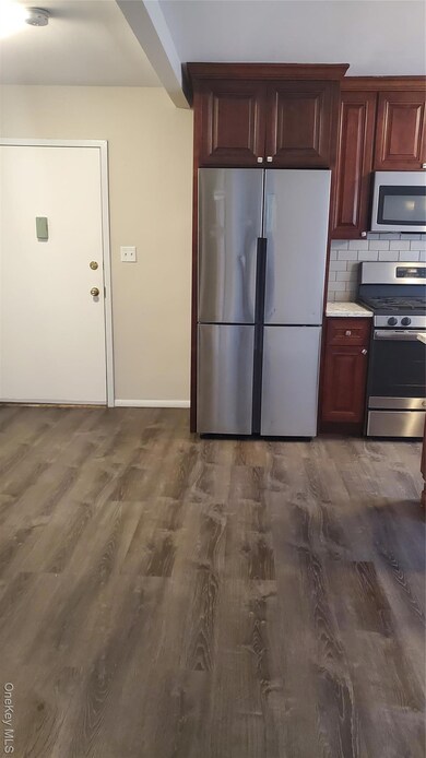 Kitchen featuring stainless steel refrigerator, range, tasteful backsplash, dark wood finished floors, and light stone countertops