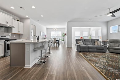 Kitchen with stainless steel range with gas stovetop, open floor plan, white cabinetry, and an island with sink