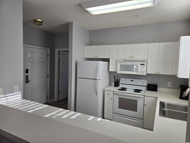 Kitchen with white appliances, light countertops, a textured ceiling, white cabinets, and a peninsula