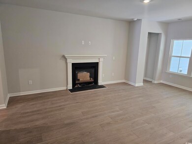 Unfurnished living room featuring wood finished floors, a fireplace with flush hearth, and baseboards