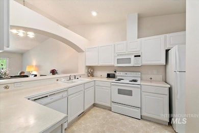 Kitchen featuring white appliances, vaulted ceiling, white cabinets, light countertops, and a textured ceiling