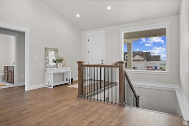 Corridor with an upstairs landing, vaulted ceiling, wood finished floors, and recessed lighting