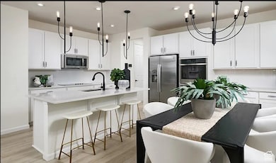 Kitchen with a kitchen bar, white cabinets, a kitchen island with sink, hanging light fixtures, and a chandelier