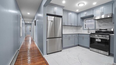 Kitchen featuring stainless steel appliances, a baseboard radiator, gray cabinets, decorative backsplash, and under cabinet range hood