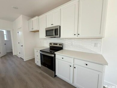 Kitchen featuring stainless steel appliances, light countertops, white cabinetry, dark wood-style floors, and decorative backsplash