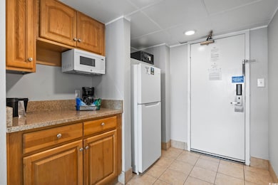 Kitchen with white appliances, brown cabinets, light tile patterned floors, and baseboards