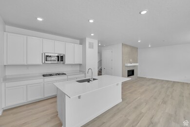 Kitchen featuring white cabinetry, light wood-type flooring, light stone counters, a kitchen island with sink, and recessed lighting