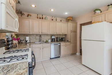 Kitchen featuring white appliances, backsplash, light tile patterned floors, recessed lighting, and light stone countertops