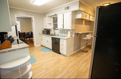 Kitchen featuring black appliances, crown molding, light wood-style floors, tasteful backsplash, and white cabinets