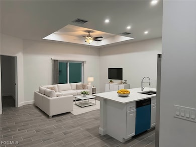 Kitchen with a tray ceiling, open floor plan, dishwashing machine, wood finish floors, and a peninsula