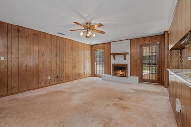 Unfurnished living room featuring wood walls, light colored carpet, a brick fireplace, and a ceiling fan