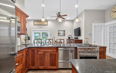 Kitchen with stainless steel appliances, a peninsula, pendant lighting, brown cabinetry, and recessed lighting