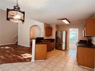 Kitchen featuring dark countertops, a peninsula, stainless steel appliances, brown cabinetry, and a textured ceiling