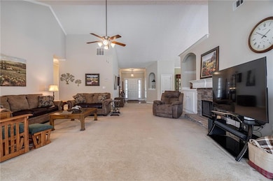 Living room featuring high vaulted ceiling, carpet, a ceiling fan, a fireplace, and built in shelves