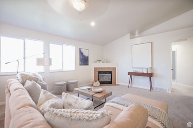 Living area featuring lofted ceiling, arched walkways, a tile fireplace, and carpet