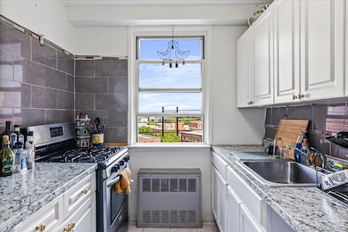 Kitchen featuring stainless steel gas range, radiator heating unit, a sink, white cabinets, and backsplash