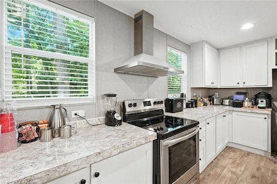 Kitchen featuring wall chimney exhaust hood, electric range, light countertops, white cabinetry, and light wood-style flooring