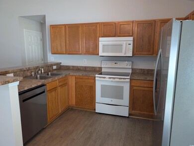 Kitchen featuring appliances with stainless steel finishes, dark wood-type flooring, dark countertops, and brown cabinets