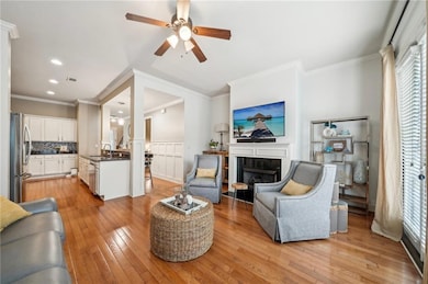 Living room with light wood-style flooring, a ceiling fan, a fireplace, recessed lighting, and ornamental molding