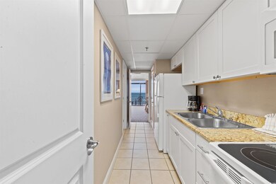 Kitchen featuring white refrigerator, a paneled ceiling, sink, light tile patterned floors, and white cabinetry