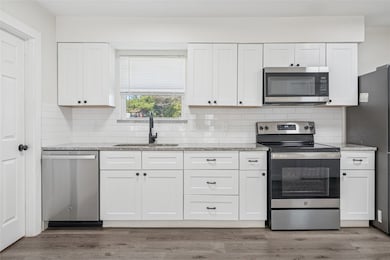 Kitchen featuring stainless steel appliances, light stone countertops, decorative backsplash, and white cabinetry