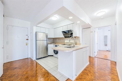 Kitchen with freestanding refrigerator, light countertops, backsplash, a peninsula, and white cabinetry