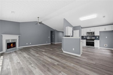 Unfurnished living room with ceiling fan, light wood-style flooring, lofted ceiling, and a fireplace