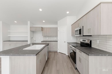 Kitchen with stainless steel appliances, light wood-style flooring, open shelves, an island with sink, and tasteful backsplash
