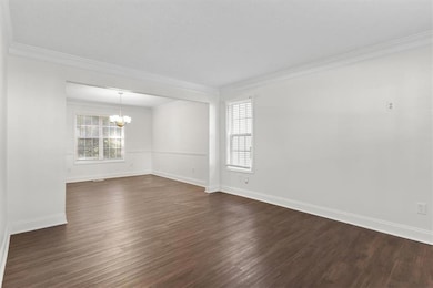 Empty room with dark wood-style floors, crown molding, and a chandelier