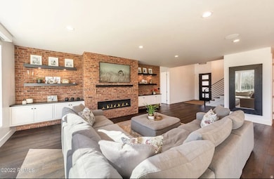 Living area with brick wall, recessed lighting, a fireplace, dark wood-style flooring, and stairway