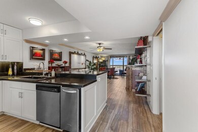 Kitchen featuring a peninsula, stainless steel dishwasher, light wood-style flooring, a sink, and dark countertops