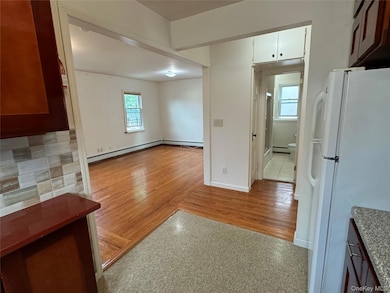 Kitchen featuring freestanding refrigerator, wood finished floors, a baseboard radiator, and brown cabinets