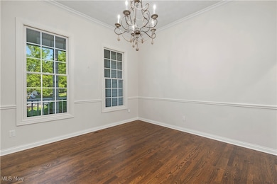 Spare room with a chandelier, dark wood finished floors, and ornamental molding