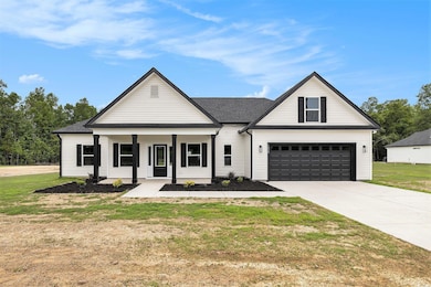 Modern farmhouse featuring concrete driveway, covered porch, a front lawn, and an attached garage