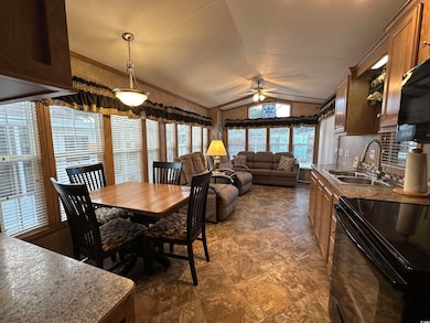 Dining room with vaulted ceiling, a ceiling fan, dark stone finish flooring, and a textured ceiling