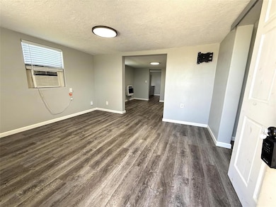 Unfurnished room with dark wood-type flooring, baseboards, a textured ceiling, and heating unit