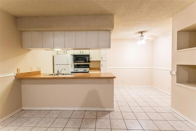 Kitchen with white appliances, a peninsula, a textured ceiling, light tile patterned flooring, and ceiling fan
