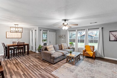 Living room with wood-type flooring, ceiling fan with notable chandelier, and a textured ceiling