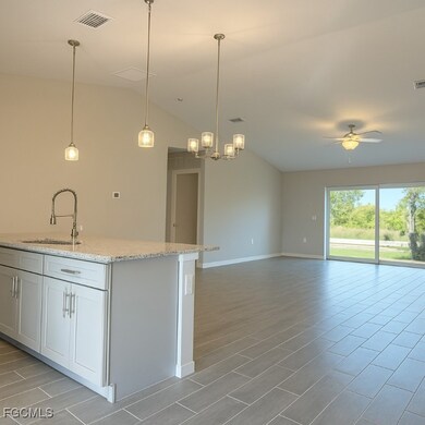 Kitchen with light stone countertops, vaulted ceiling, open floor plan, a kitchen island with sink, and wood finish floors